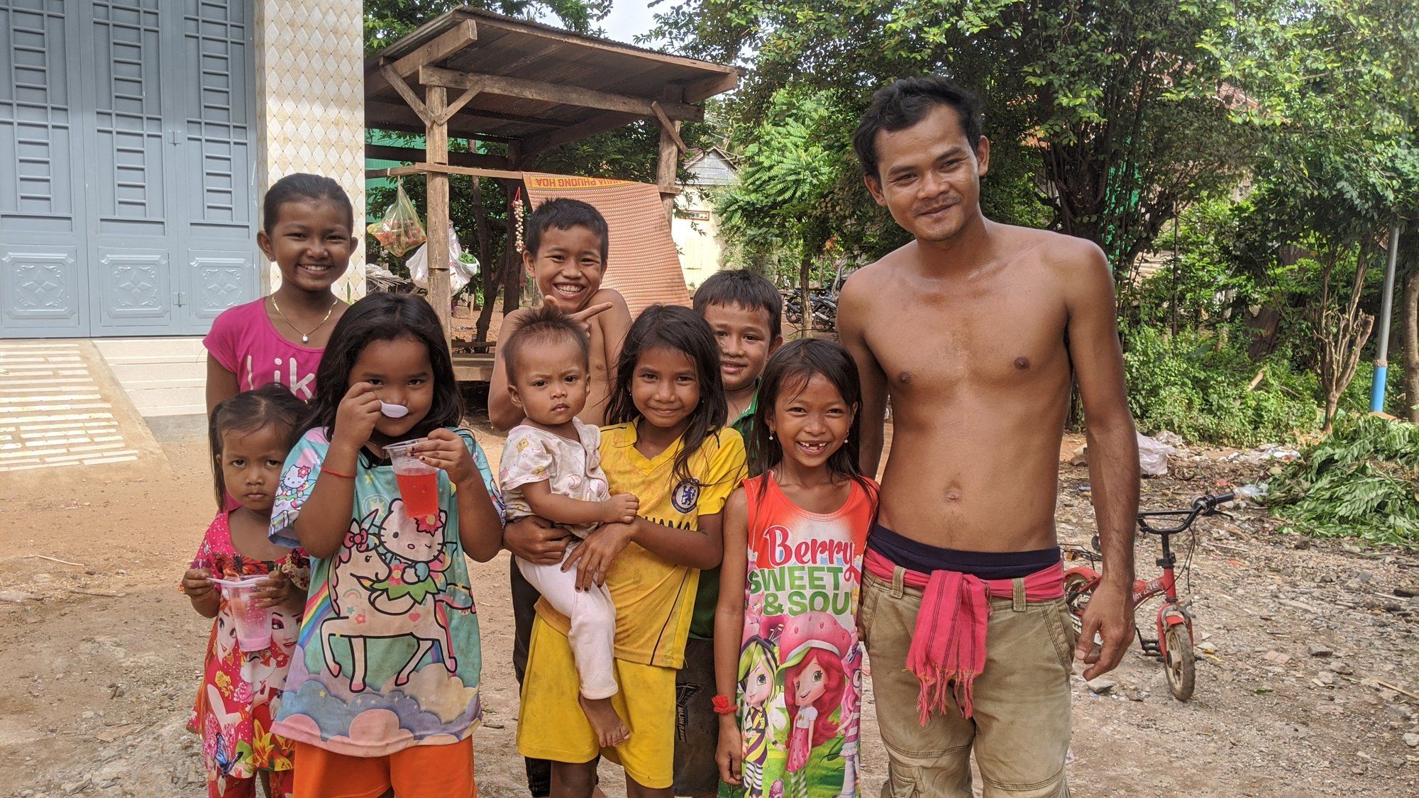 A village family of eight, from a toddler to a young father, posing together outside their home