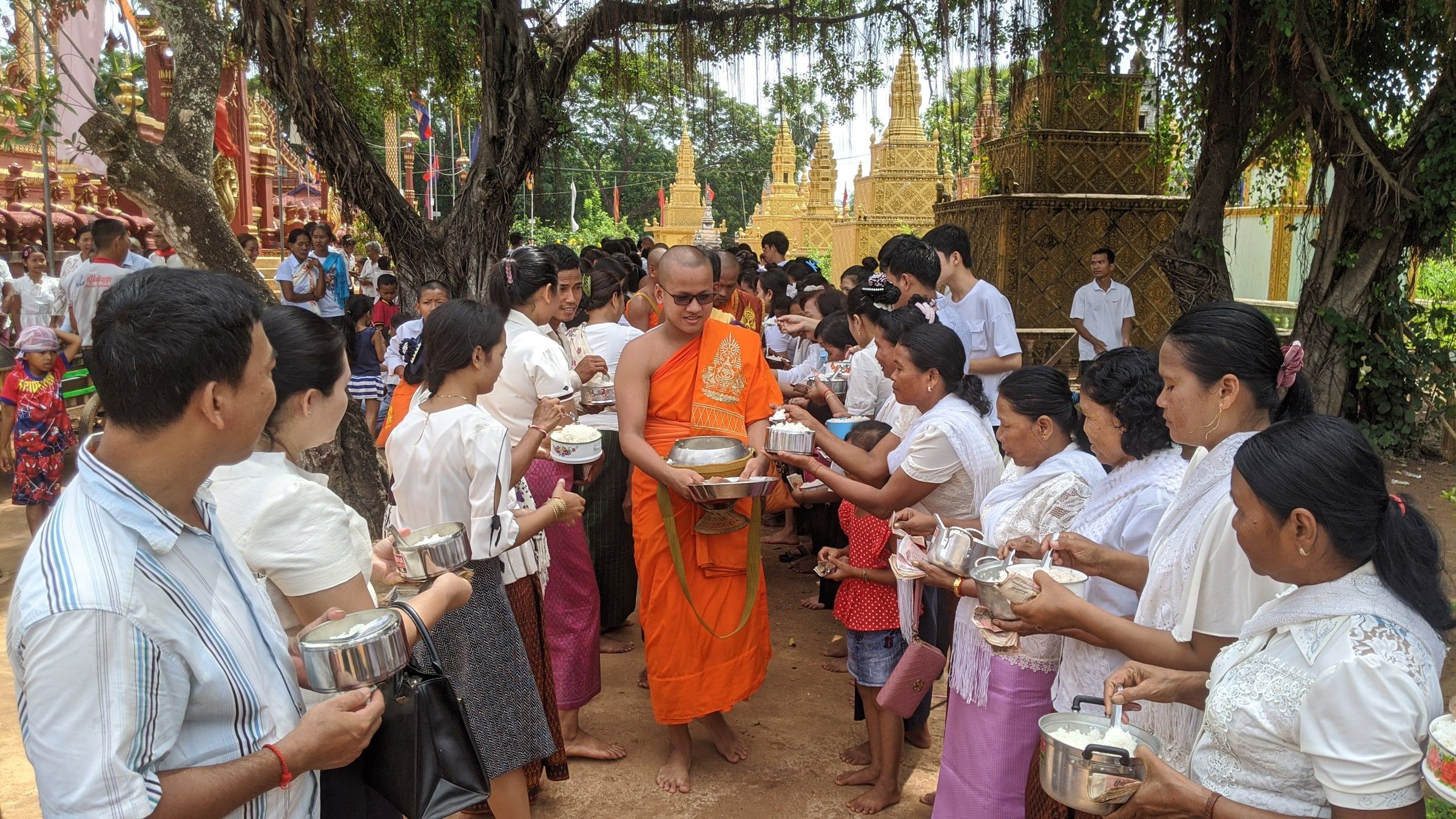 Villagers in white offering food to a monk in saffron robes at a pagoda ceremony