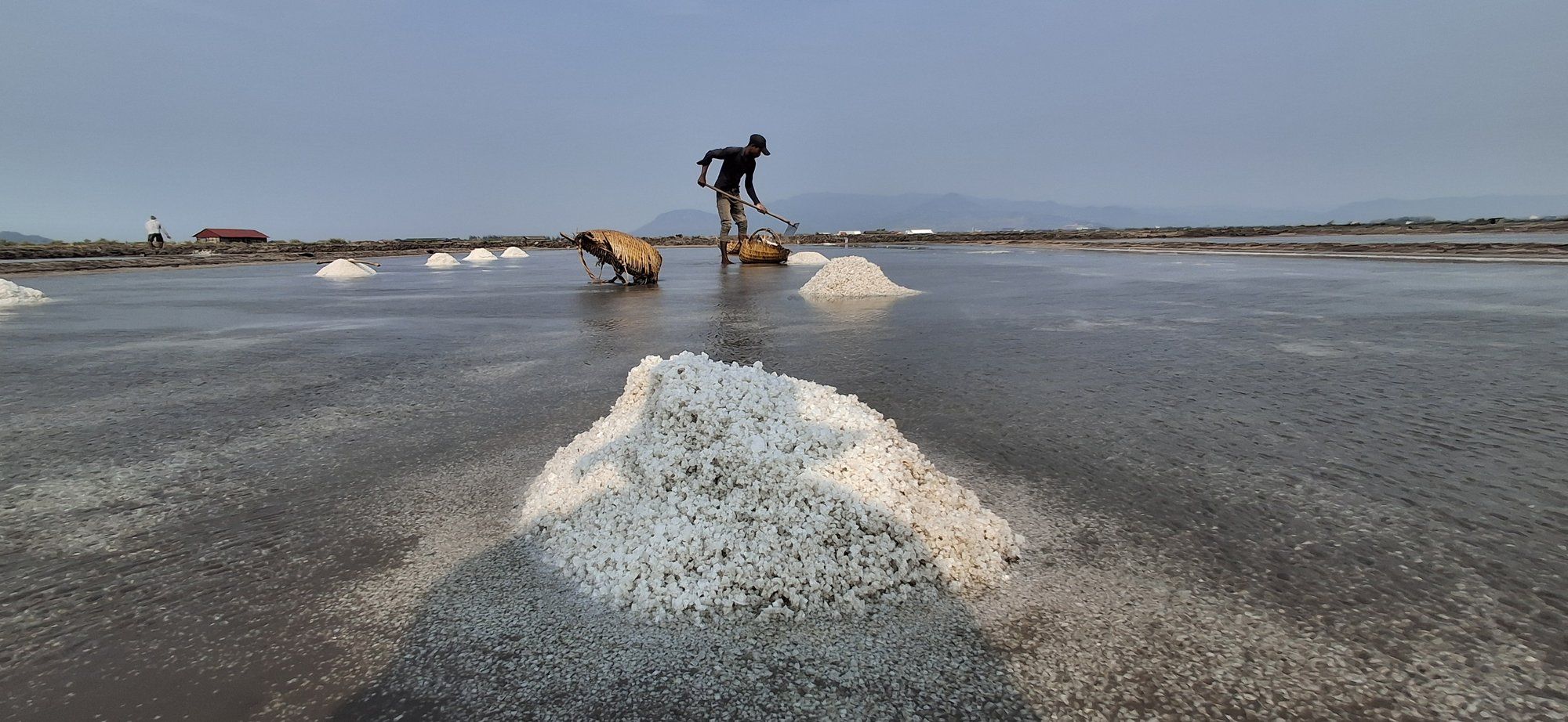 A mound of raked salt in the foreground, with a worker and the Elephant Mountains behind