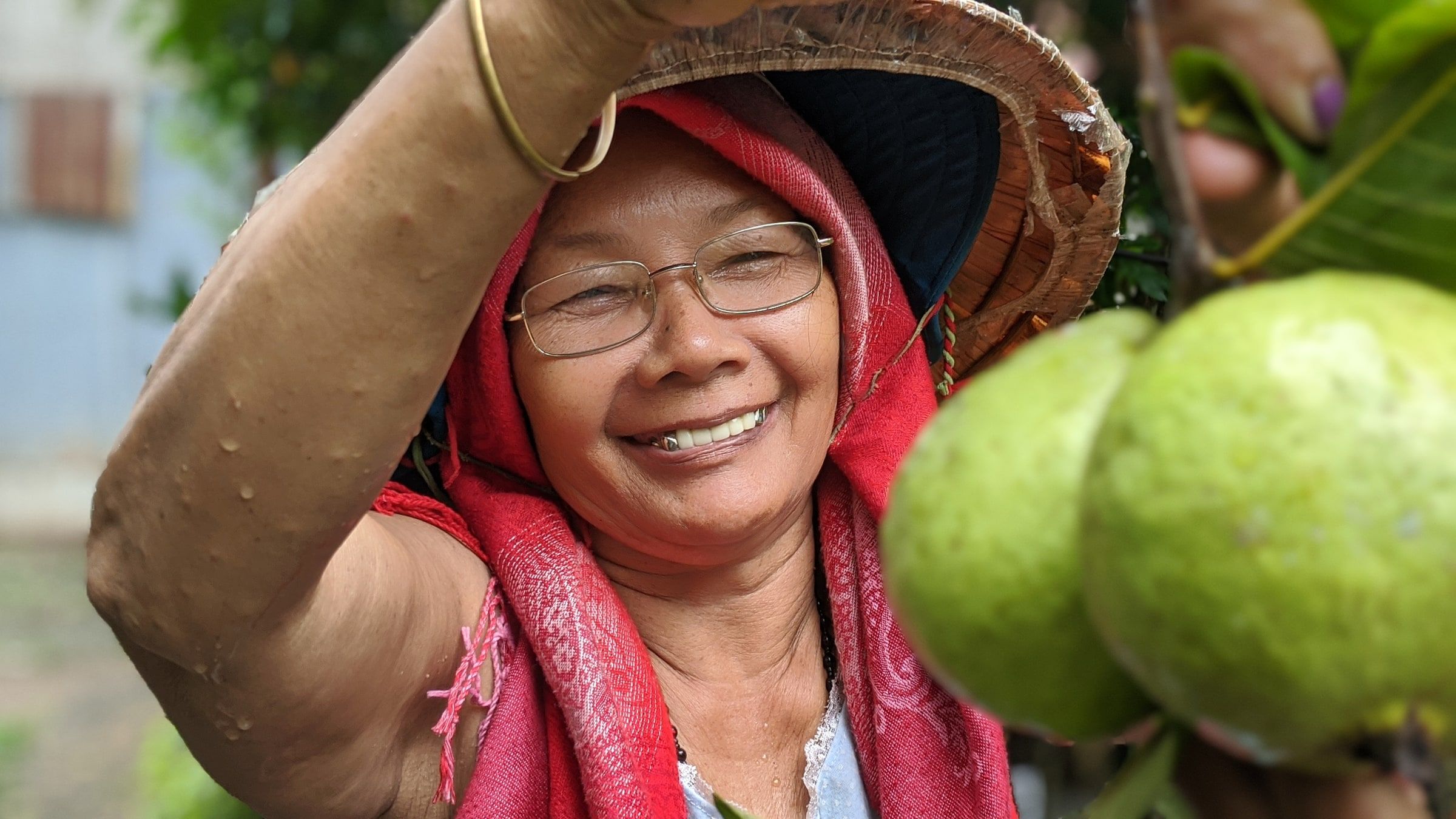 A smiling woman in a sun hat reaching up to pick fruit